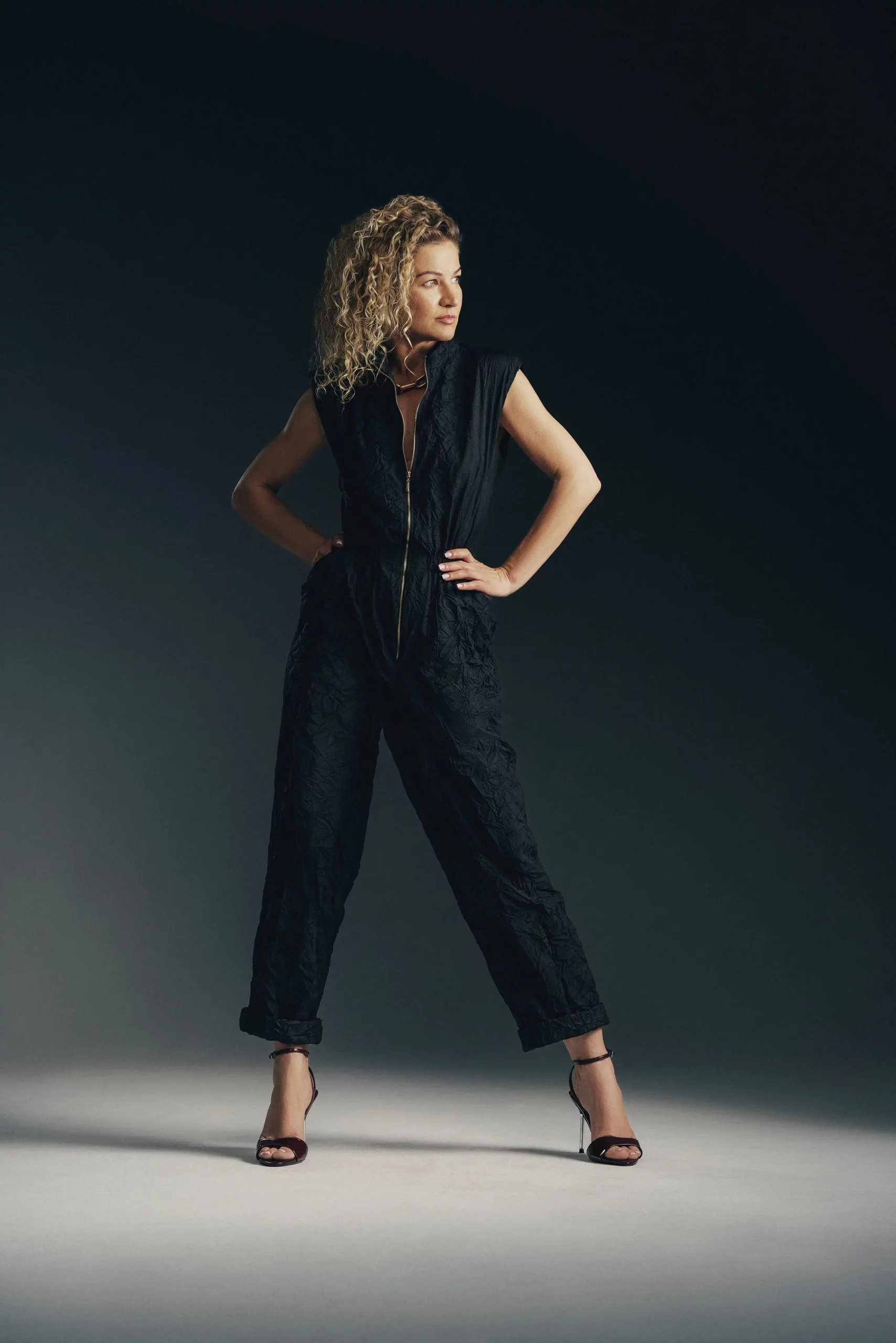 Modelka w czarnym eleganckim kombinezonie bez rękawów z zamkiem i szpilkami – stylowa sesja w studio