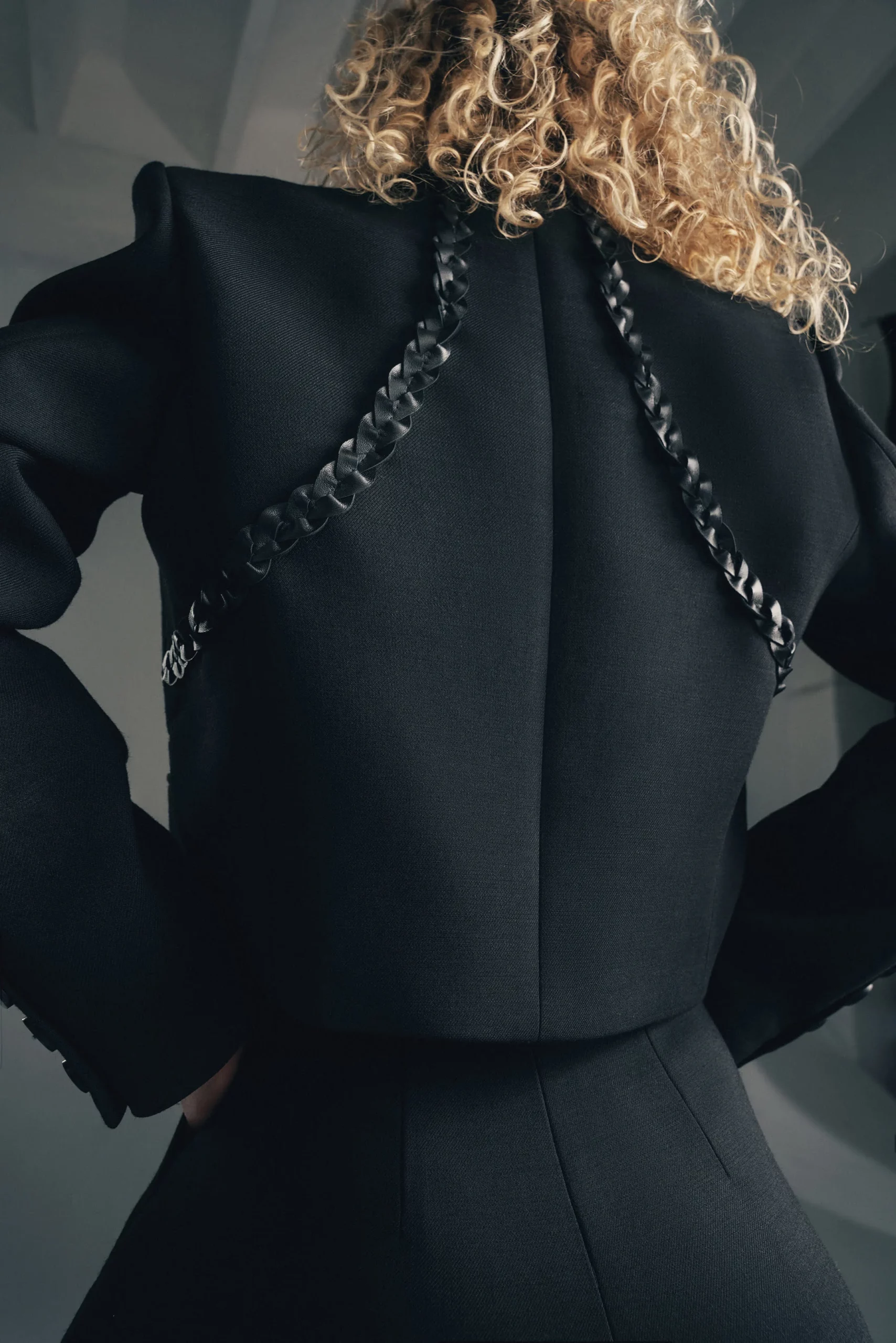 Modelka w czarnej marynarce Marry z ozdobnym plecionym skórzanym warkoczem z tyłu – nowoczesny, kobiecy look. Krótka czarna marynarka damska