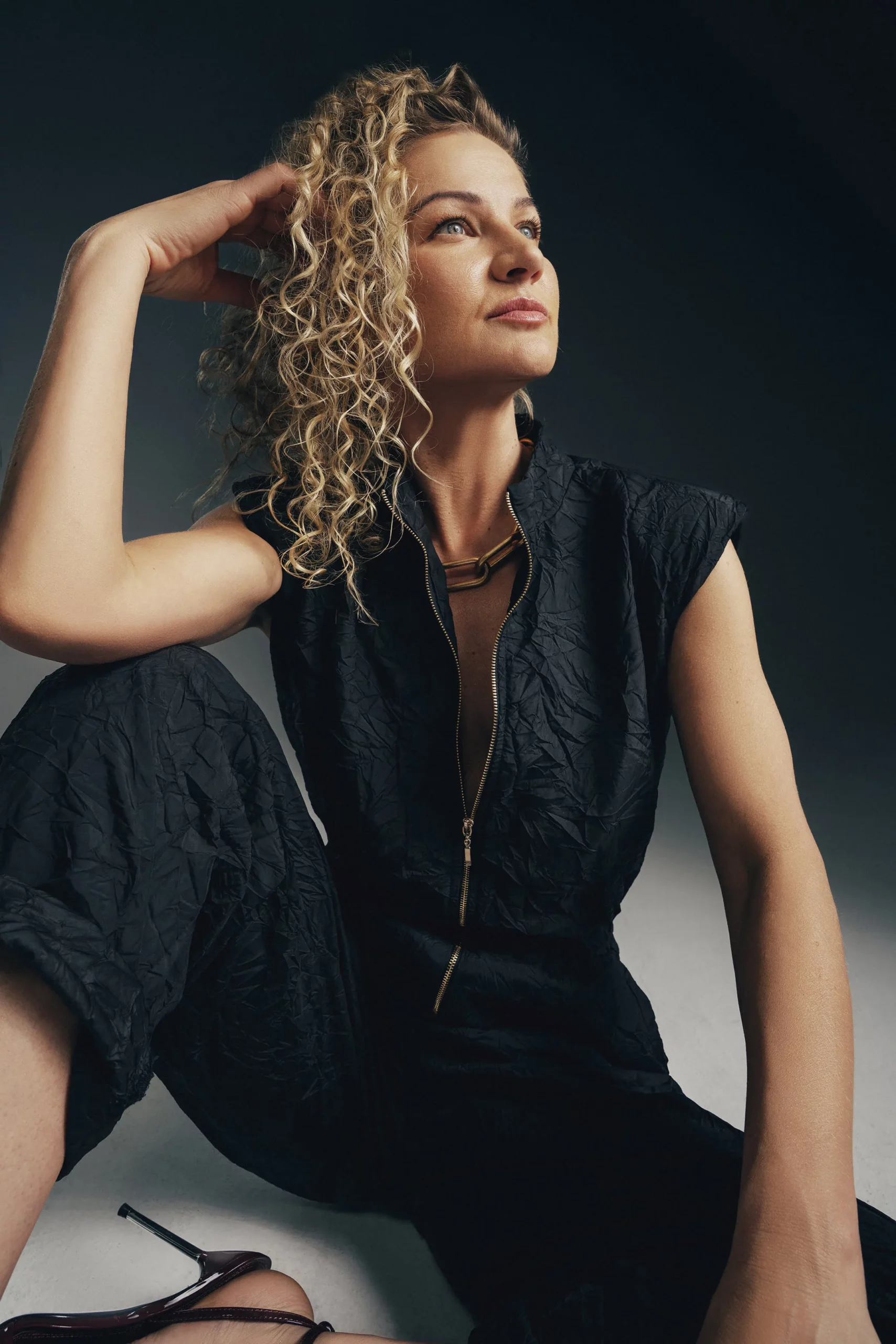 Modelka w czarnym eleganckim kombinezonie bez rękawów z zamkiem i szpilkami – stylowa sesja w studio